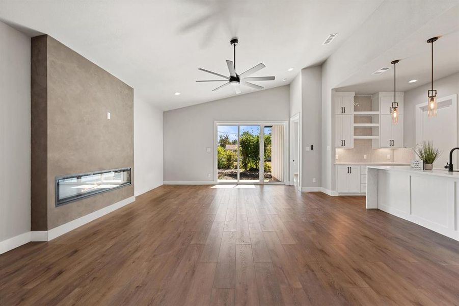 Kitchen featuring hanging light fixtures, open floor plan, wood finished floors, lofted ceiling, and light stone countertops Kitchen featuring hanging light fixtures, open floor plan, wood finished floors, lofted ceiling, and light stone countertops