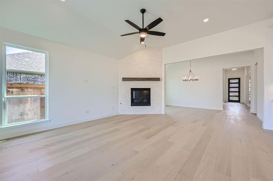 Unfurnished living room featuring ceiling fan with notable chandelier, lofted ceiling, light hardwood / wood-style floors, and a stone fireplace