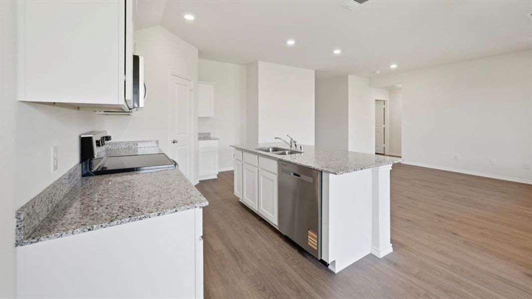 Kitchen featuring light stone counters, white cabinetry, dark wood-type flooring, a center island with sink, and black electric range