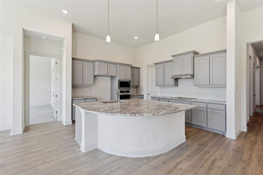 Kitchen with gray cabinets, decorative light fixtures, light stone countertops, light wood-style flooring, and recessed lighting Kitchen with gray cabinets, decorative light fixtures, light stone countertops, light wood-style flooring, and recessed lighting