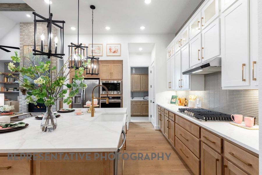 Kitchen with under cabinet range hood, stainless steel appliances, backsplash, light wood-style floors, and decorative light fixtures Kitchen with under cabinet range hood, stainless steel appliances, backsplash, light wood-style floors, and decorative light fixtures