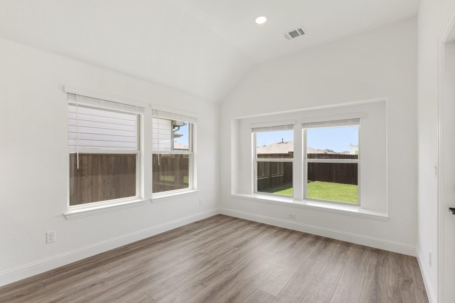 Empty room with vaulted ceiling, wood-look floors, and three windows overlooking a backyard Empty room with vaulted ceiling, wood-look floors, and three windows overlooking a backyard