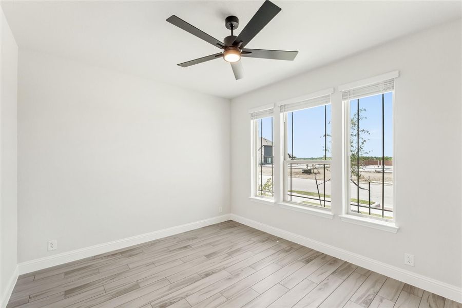 Empty room with light wood floors, ceiling fan, and two windows with neighborhood view