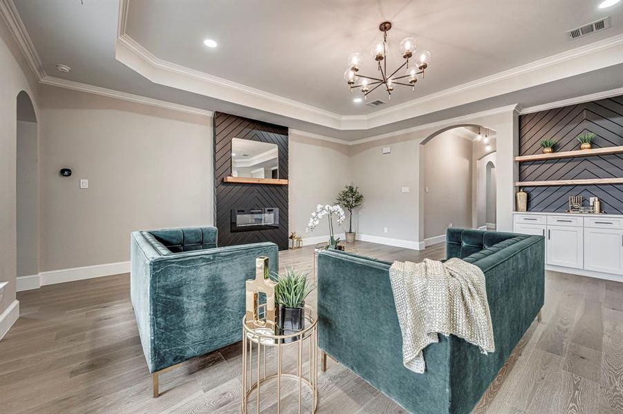 Living room featuring a raised ceiling, wood-type flooring, ornamental molding, and a fireplace