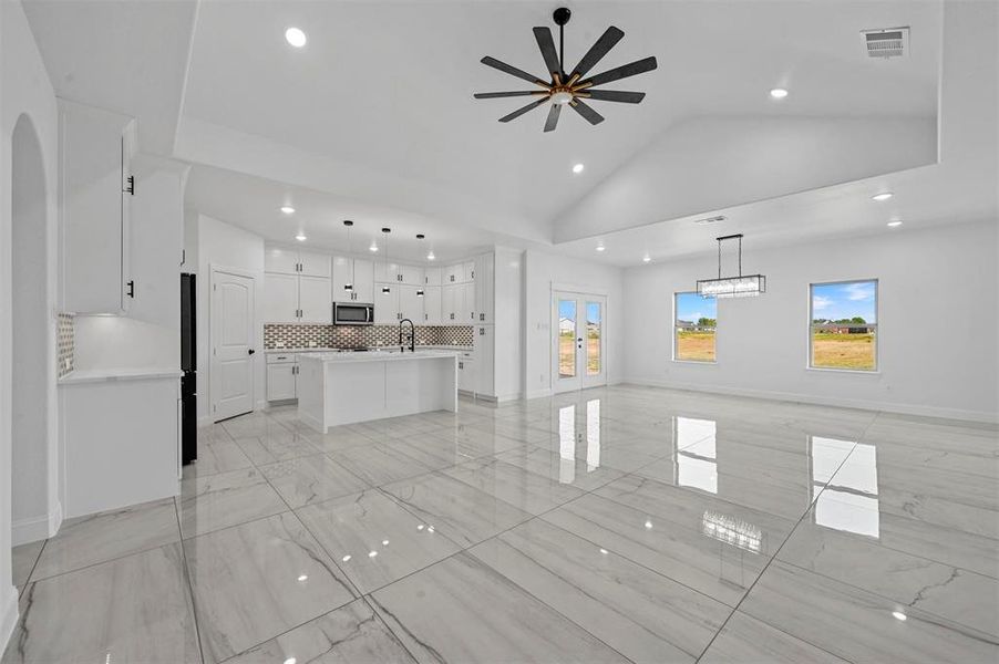 Unfurnished living room featuring ceiling fan, sink, light tile patterned floors, and high vaulted ceiling