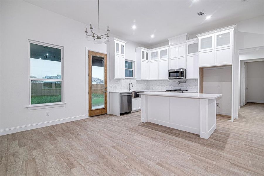 Kitchen with stainless steel appliances, light countertops, backsplash, light wood-style floors, and white cabinets Kitchen with stainless steel appliances, light countertops, backsplash, light wood-style floors, and white cabinets