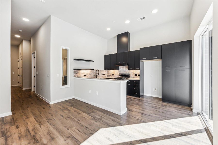 A contemporary kitchen space boasts high ceilings, sleek cabinetry, and rich hardwood flooring. A contemporary kitchen space boasts high ceilings, sleek cabinetry, and rich hardwood flooring.