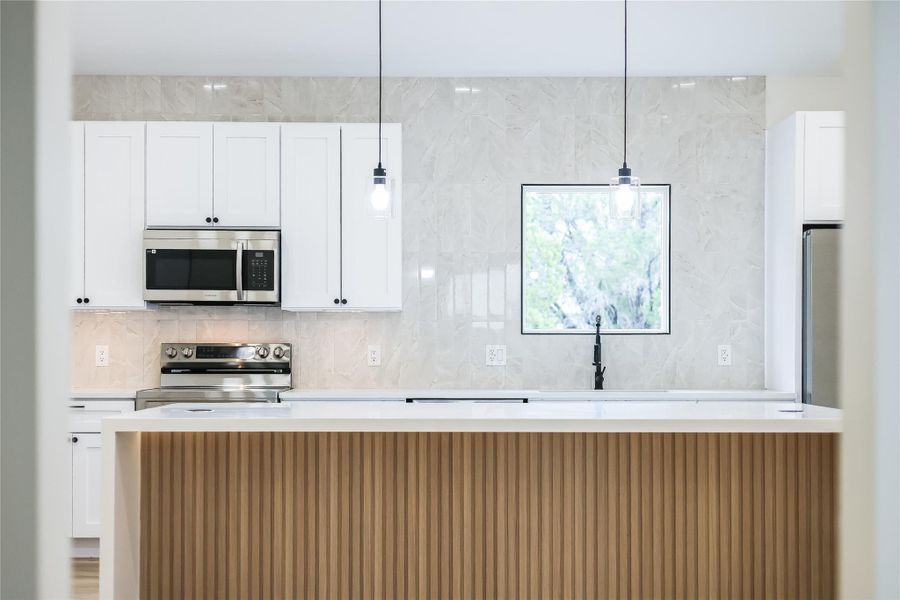 Kitchen with stainless steel appliances, light countertops, white cabinetry, and pendant lighting Kitchen with stainless steel appliances, light countertops, white cabinetry, and pendant lighting