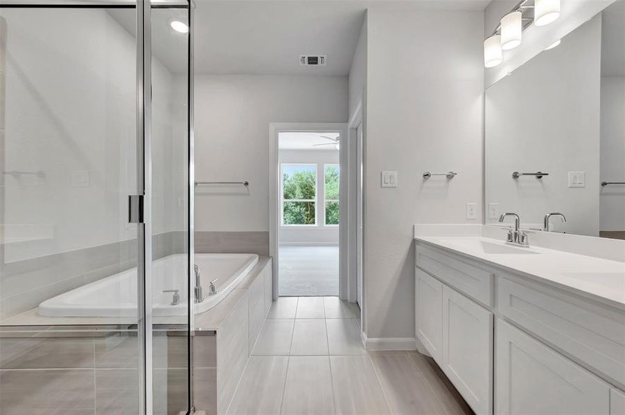 Bathroom featuring a dual vanity with white cabinetry and countertops, a large mirror with a three-light fixture, a built-in tub, and a separate glass-enclosed shower
