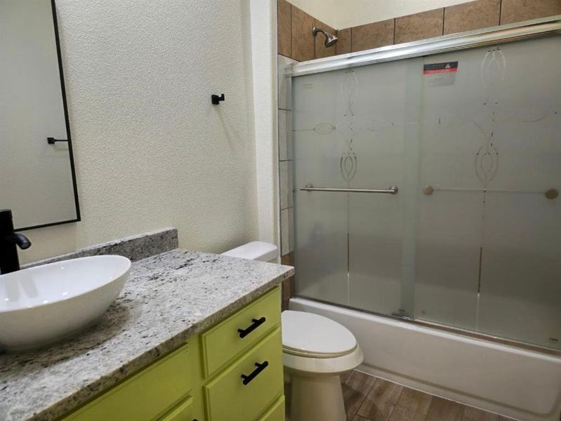 Full bathroom featuring toilet, vanity, wood-type flooring, and combined bath / shower with glass door