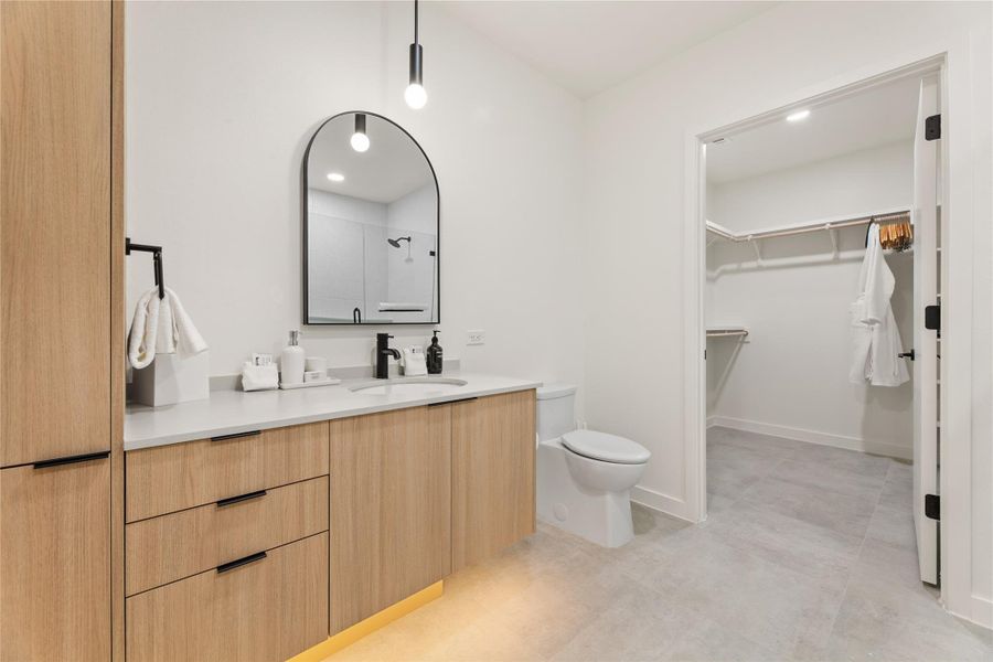 Minimalist cabinetry and sleek stone counters define this modern bathroom with adjoining walk-in closet.