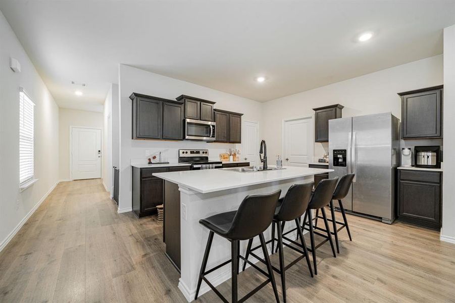 Kitchen featuring appliances with stainless steel finishes, light wood-type flooring, a kitchen island with sink, a kitchen bar, and recessed lighting Kitchen featuring appliances with stainless steel finishes, light wood-type flooring, a kitchen island with sink, a kitchen bar, and recessed lighting