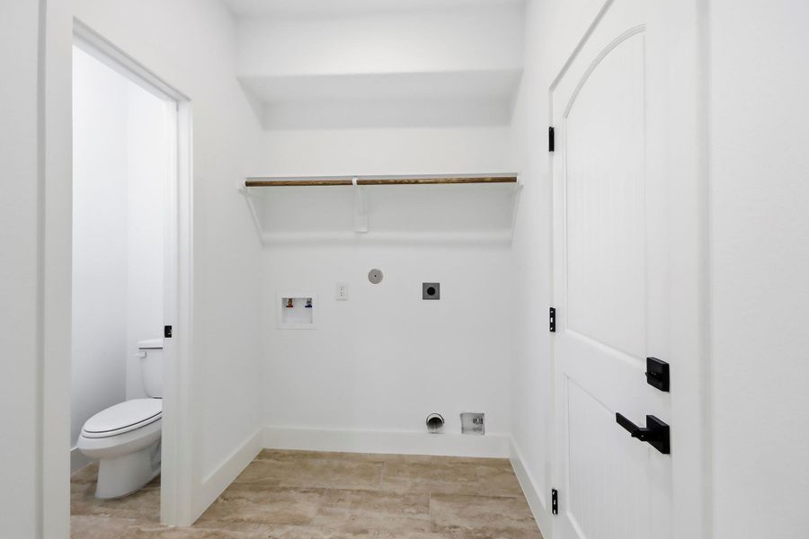 Spacious laundry room with built-in shelving and convenient adjacent half bath, featuring modern fixtures and ample storage potential.