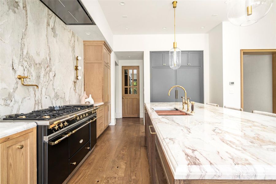 An expansive natural stone island takes center stage in the kitchen, complemented by custom white oak cabinetry, warm brass details, and a dramatic full-height stone backsplash. Thoughtfully layered materials give the space a refined, collected feel while maintaining the warmth that carries throughout the home. An expansive natural stone island takes center stage in the kitchen, complemented by custom white oak cabinetry, warm brass details, and a dramatic full-height stone backsplash. Thoughtfully layered materials give the space a refined, collected feel while maintaining the warmth that carries throughout the home.