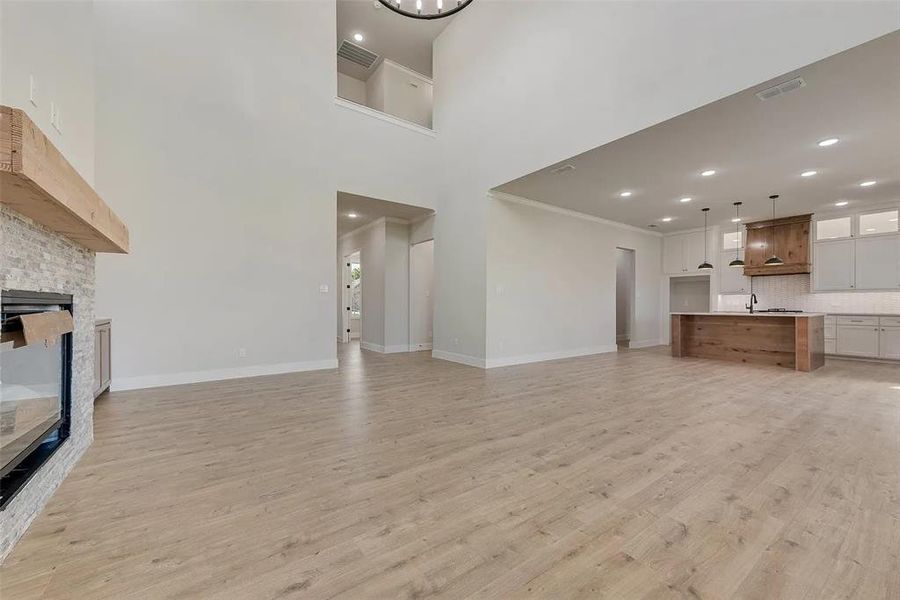 Unfurnished living room with a fireplace, light wood finished floors, suspended lighting, and crown molding