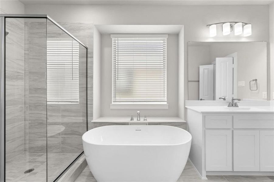 Freestanding soaking tub, glass-enclosed shower with tiled surround, dual vanity with white cabinetry, and contemporary lighting fixture Freestanding soaking tub, glass-enclosed shower with tiled surround, dual vanity with white cabinetry, and contemporary lighting fixture