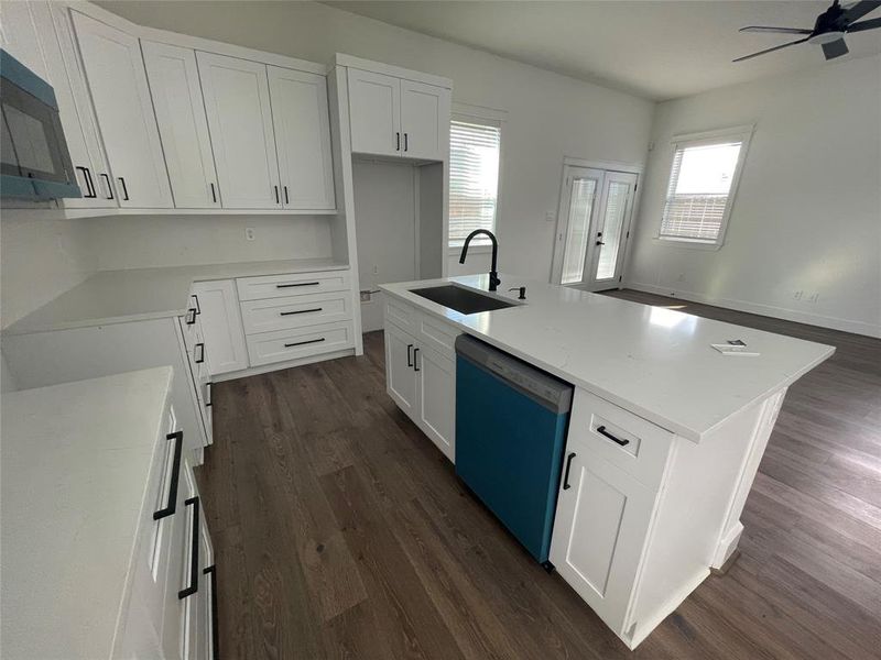 Kitchen featuring a center island with sink, dark wood-type flooring, white cabinetry, dishwashing machine, and light stone counters