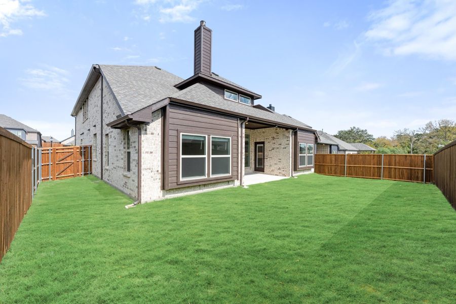 Rear exterior of brick home with chimney, covered patio, and fenced backyard with green lawn