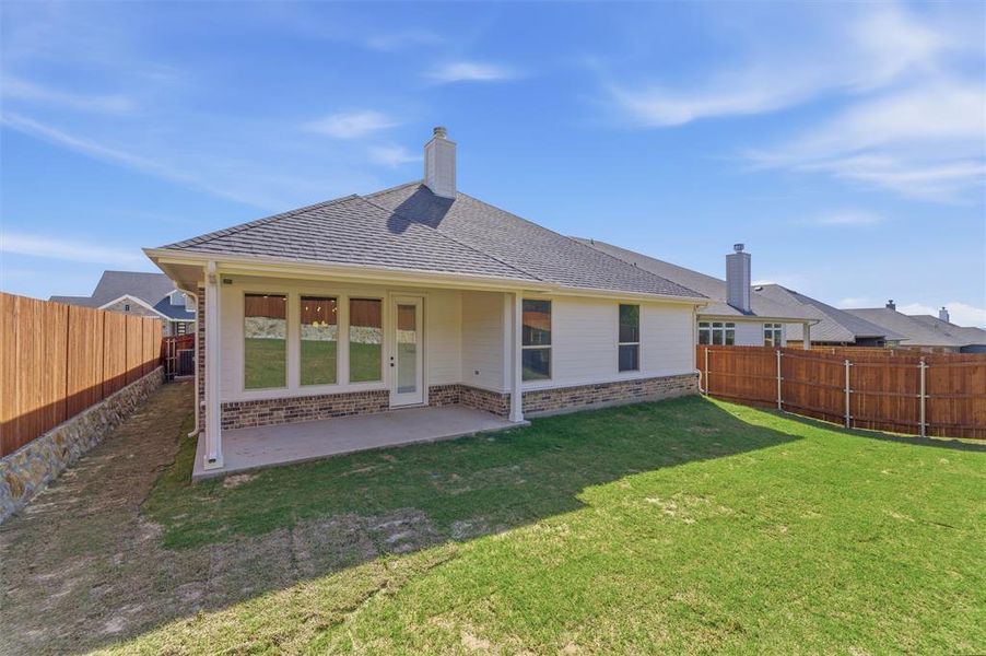 Rear view of house with brick siding, a fenced backyard, a shingled roof, and a patio area