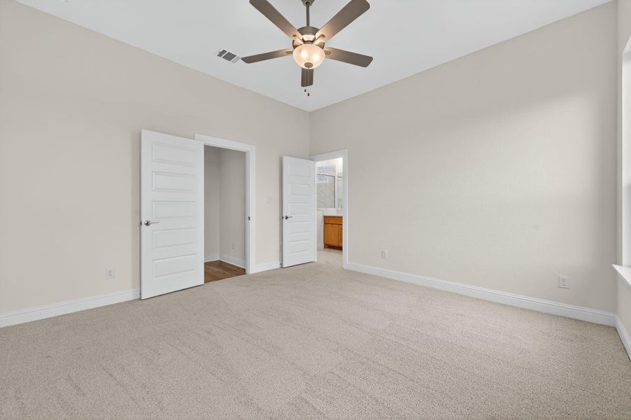 Unfurnished bedroom featuring light carpet, ensuite bath, and ceiling fan