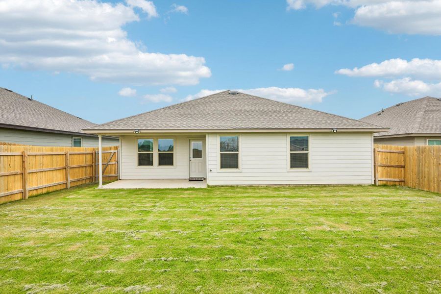 Expansive backyard with a covered concrete patio, wood privacy fencing, and a manicured lawn
