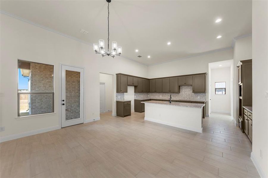 Kitchen with crown molding, an island with sink, a chandelier, open floor plan, and tasteful backsplash Kitchen with crown molding, an island with sink, a chandelier, open floor plan, and tasteful backsplash