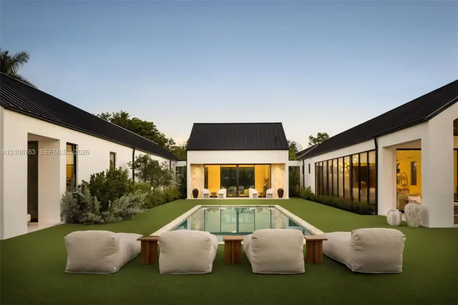 Courtyard featuring a swimming pool, synthetic lawn, dark metal roof, and stone-accented exterior wall