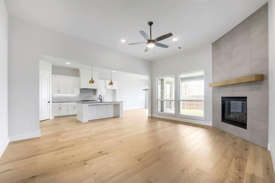 Spacious interior featuring light wood-finish flooring, a tiled fireplace with a wood mantel, a ceiling fan, and large windows
