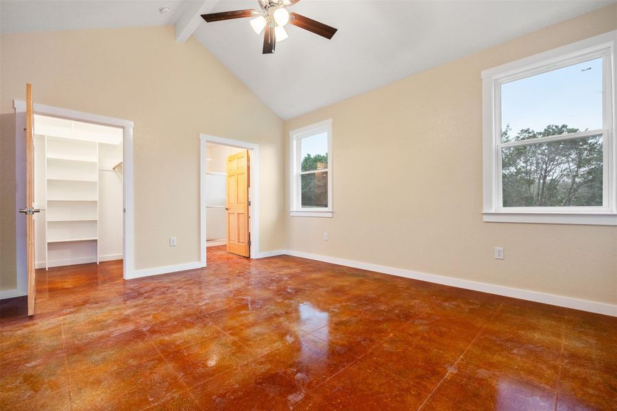 Unfurnished bedroom featuring a walk in closet, beam ceiling, a ceiling fan, and high vaulted ceiling