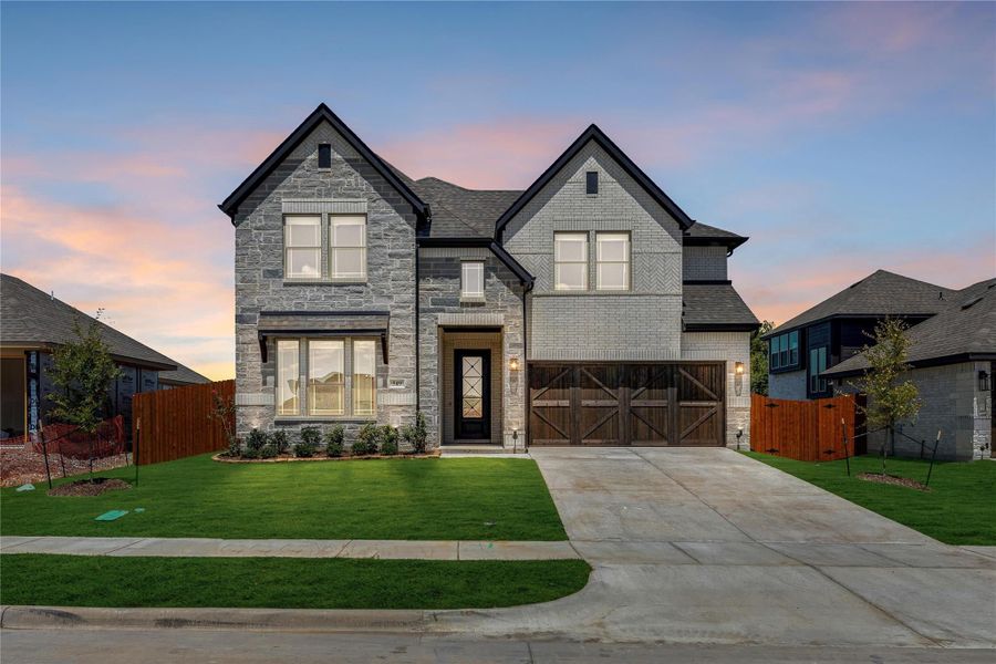Two-story home with stone and brick exterior, wood garage doors, and manicured front lawn at dusk