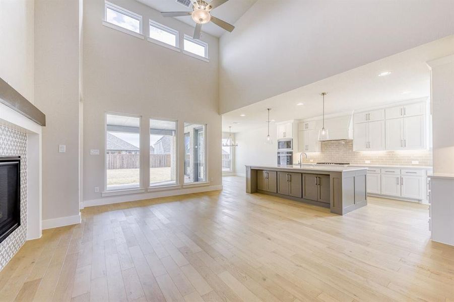 Unfurnished living room featuring a tiled fireplace, a ceiling fan, light wood-style flooring, and a high ceiling