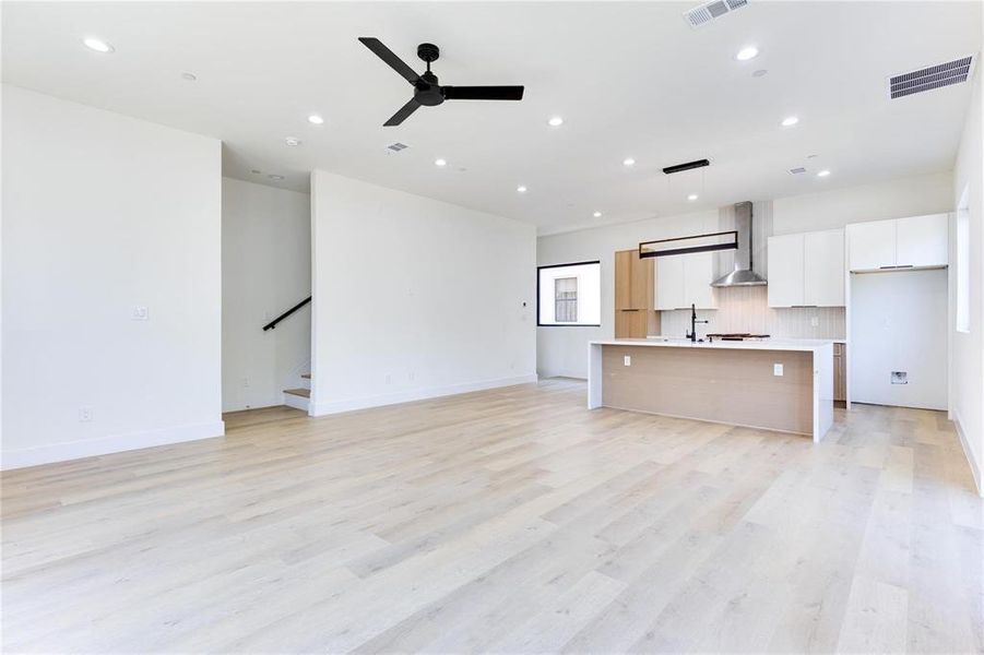 Kitchen with decorative light fixtures, white cabinetry, a kitchen island with sink, ceiling fan, and wall chimney range hood