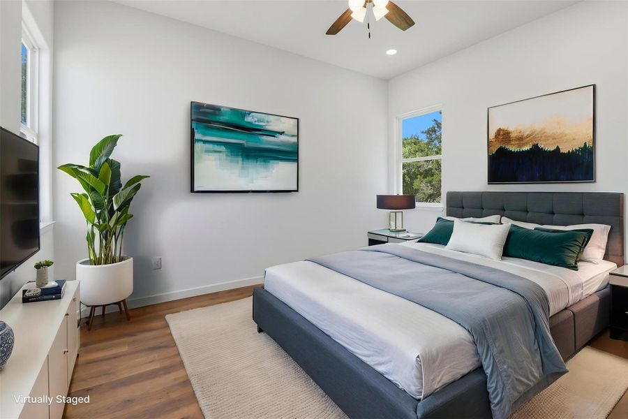 Spacious room featuring wood-finish flooring, two large windows, a ceiling fan with integrated lighting, and white walls Spacious room featuring wood-finish flooring, two large windows, a ceiling fan with integrated lighting, and white walls