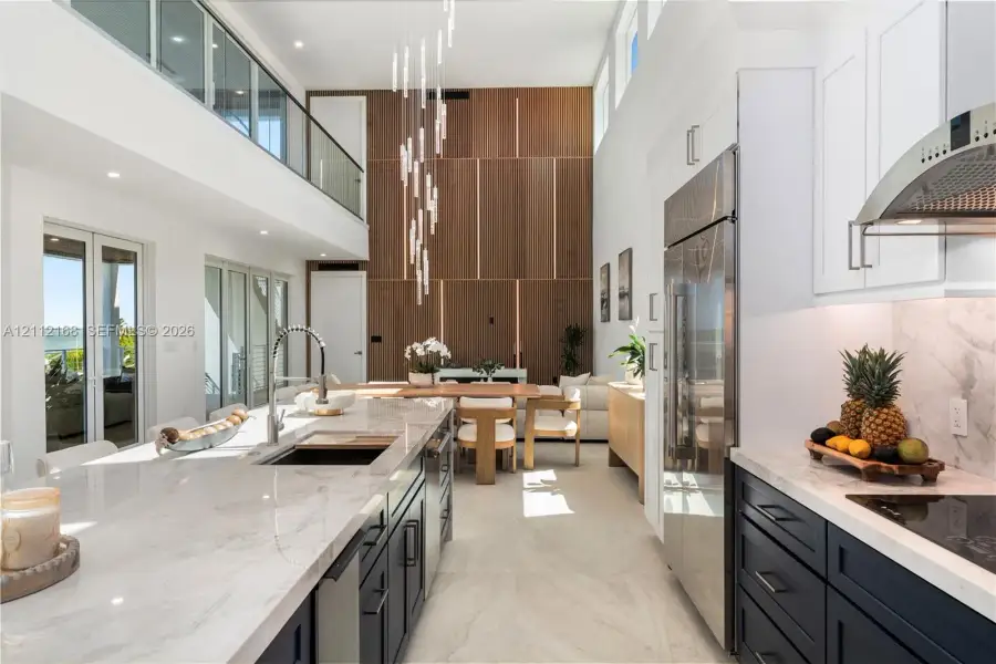 Double-height ceilings, floor-to-ceiling wood-panel accent wall, dual-tone cabinetry with stone-finish countertops, stainless steel integrated appliances, and glass-railing mezzanine Double-height ceilings, floor-to-ceiling wood-panel accent wall, dual-tone cabinetry with stone-finish countertops, stainless steel integrated appliances, and glass-railing mezzanine