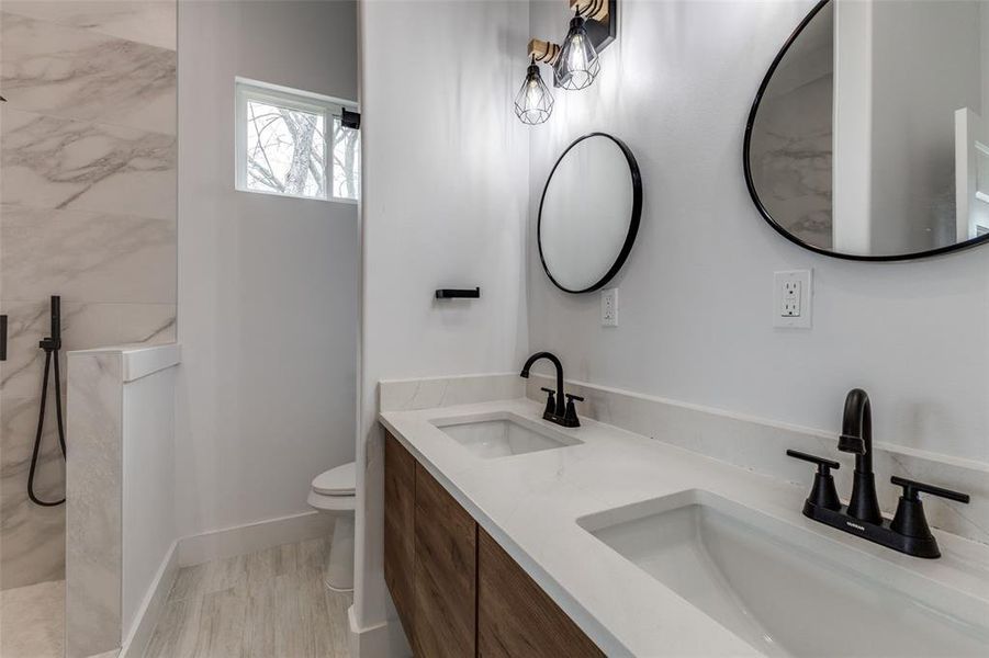 Full bathroom featuring a marble finish shower, double vanity, toilet, and a sink