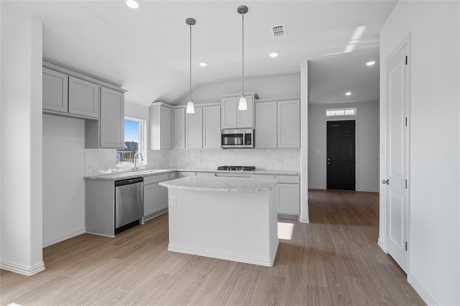 Kitchen with decorative backsplash, vaulted ceiling, light wood-type flooring, a center island, and decorative light fixtures Kitchen with decorative backsplash, vaulted ceiling, light wood-type flooring, a center island, and decorative light fixtures