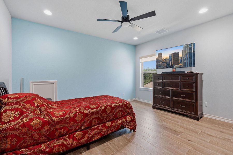 Recessed lighting and a ceiling fan illuminate this spacious bedroom with wood-look tile flooring. Recessed lighting and a ceiling fan illuminate this spacious bedroom with wood-look tile flooring.