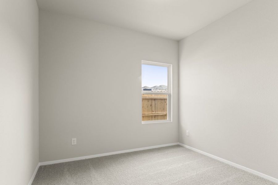 Image of a bedroom with tan carpeting, light grey walls and a window