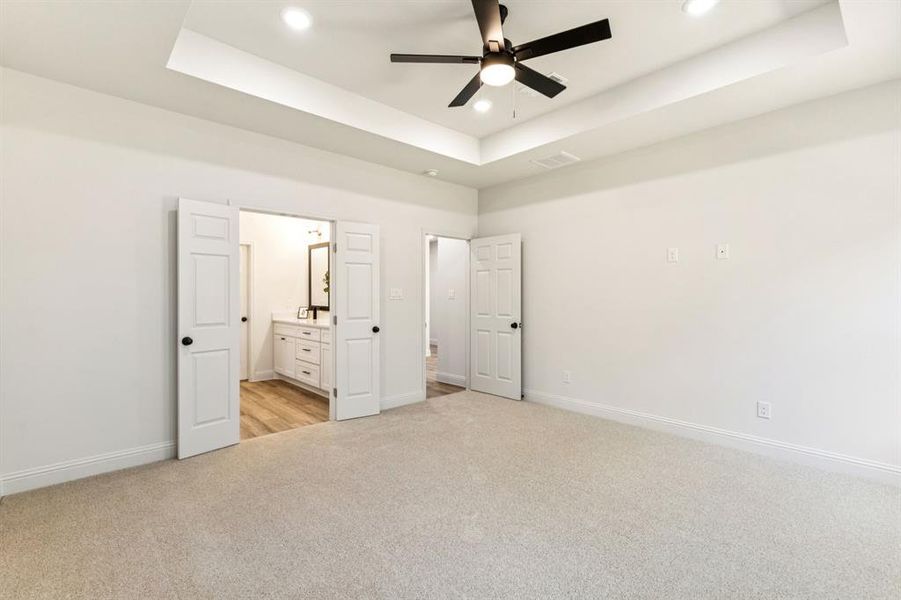 Unfurnished bedroom with a tray ceiling, light carpet, ensuite bathroom, ceiling fan, and recessed lighting