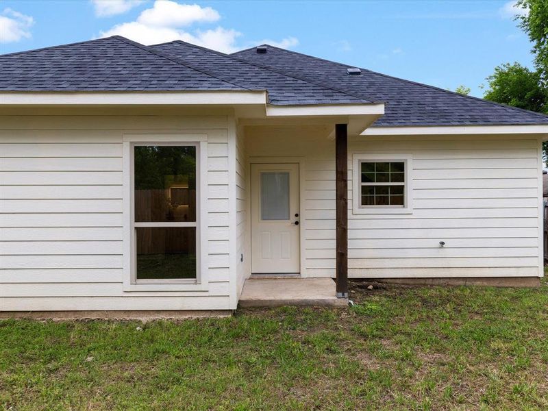 Entrance to property with roof with shingles, a yard, and a patio