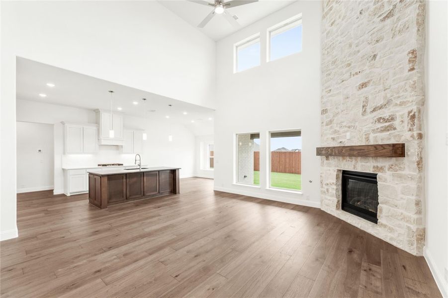 Open living area with stone fireplace, high ceilings, hardwood floors, and open kitchen with dark island in background