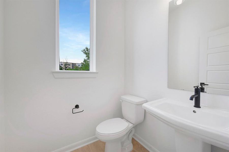 Pedestal sink featuring a matte black faucet, a vertical window, and wood-finish flooring
