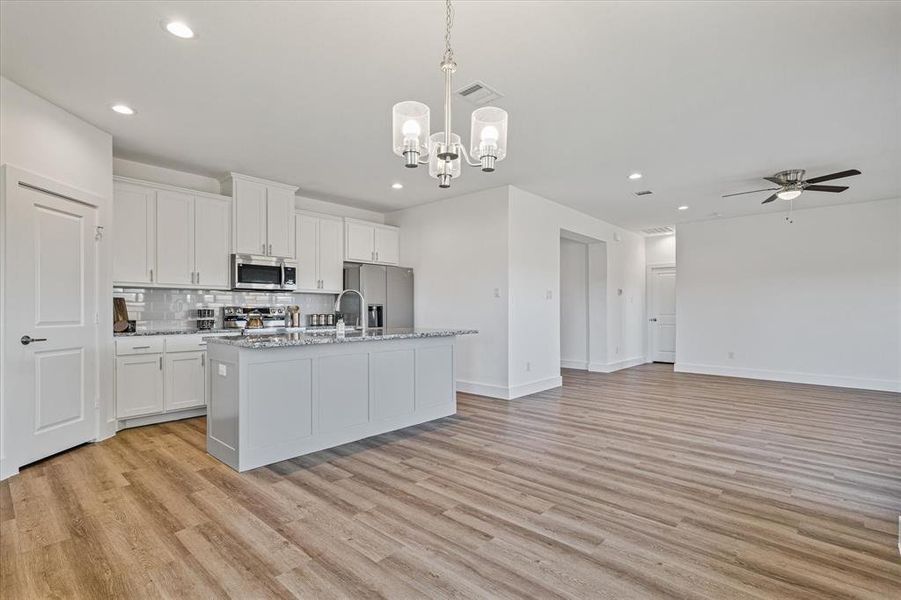 Kitchen with white cabinetry, hanging light fixtures, light hardwood / wood-style flooring, a kitchen island with sink, and appliances with stainless steel finishes Kitchen with white cabinetry, hanging light fixtures, light hardwood / wood-style flooring, a kitchen island with sink, and appliances with stainless steel finishes