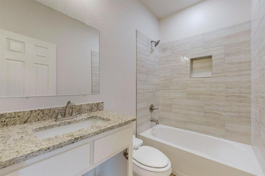 Full bathroom featuring tiled shower / bath combo, toilet, and vanity