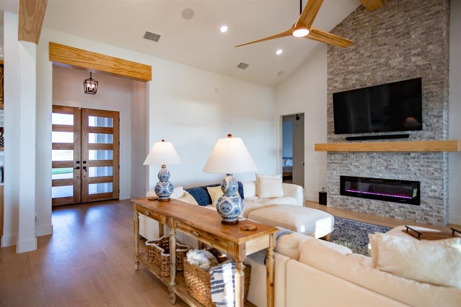 Living area featuring light wood-style flooring, high vaulted ceiling, a fireplace, recessed lighting, and a ceiling fan Living area featuring light wood-style flooring, high vaulted ceiling, a fireplace, recessed lighting, and a ceiling fan