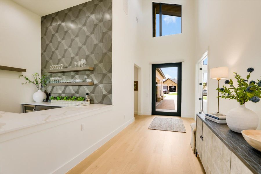 A well-lit entry hall features soaring ceilings and natural wood flooring.