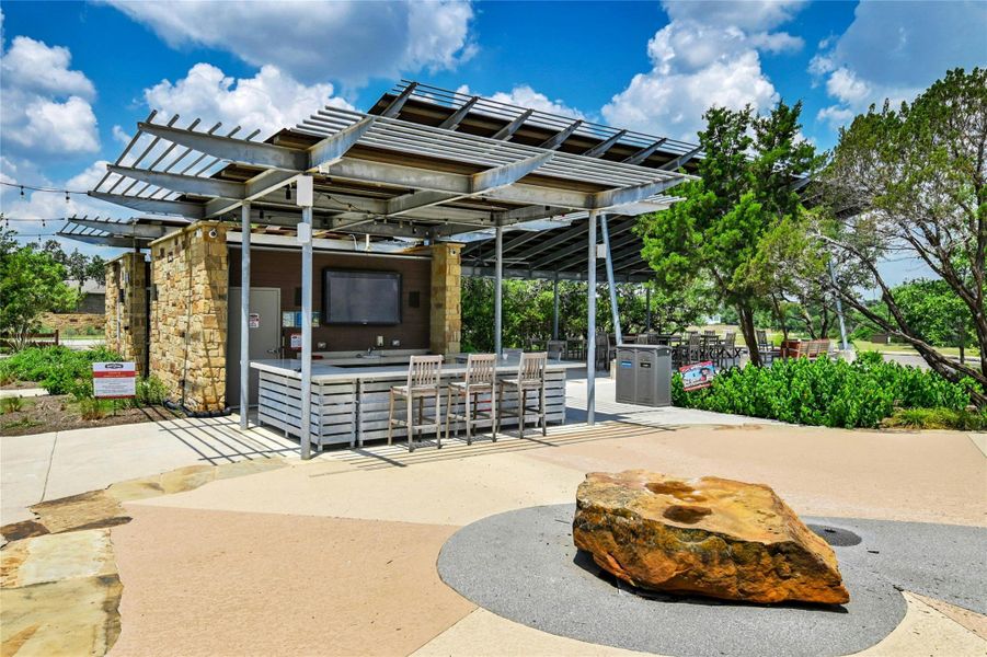 Outdoor communal space featuring a covered bar area with stone accents and a television, bar stools, and string lighting