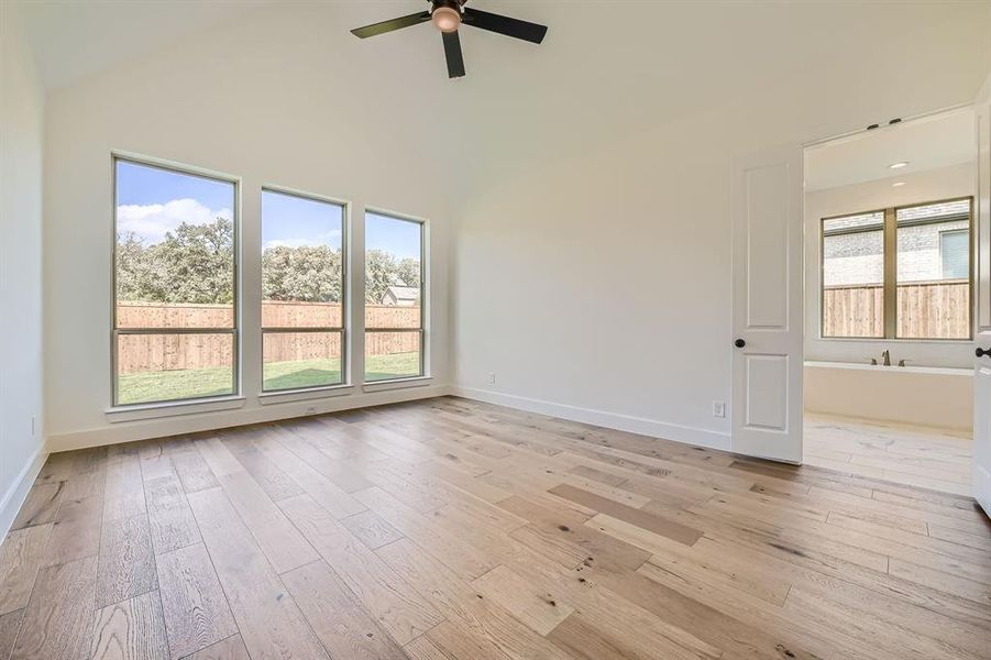 Empty room featuring ceiling fan, high vaulted ceiling, light hardwood / wood-style floors, and plenty of natural light