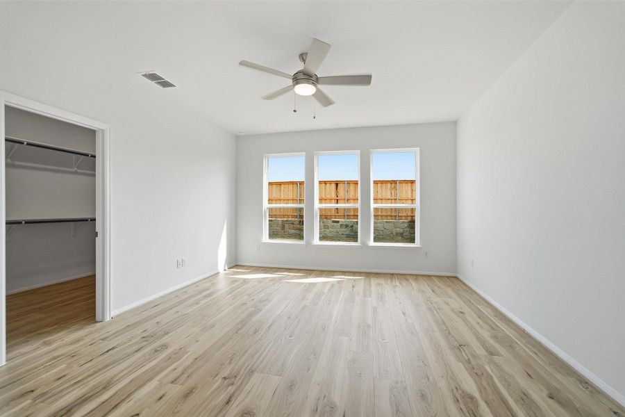 Unfurnished bedroom featuring a spacious closet, light wood finished floors, and a ceiling fan