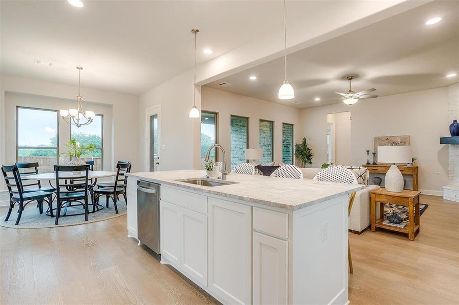 Kitchen featuring white cabinets, ceiling fan with notable chandelier, pendant lighting, a kitchen island with sink, and sink